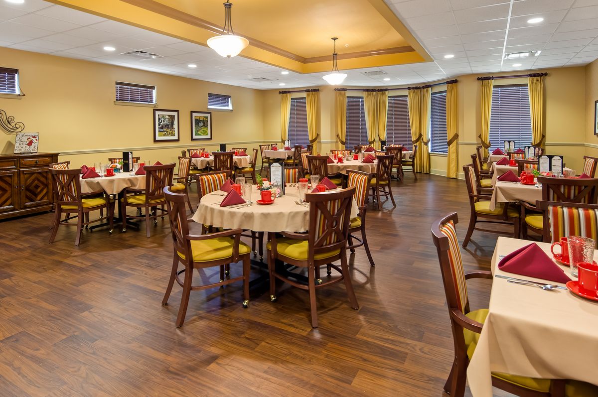 A cozy restaurant dining area with neatly arranged tables and chairs, featuring warm yellow walls and elegant wooden flooring.