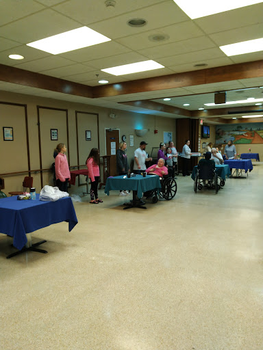 A community event taking place with participants gathered around tables, some in wheelchairs.