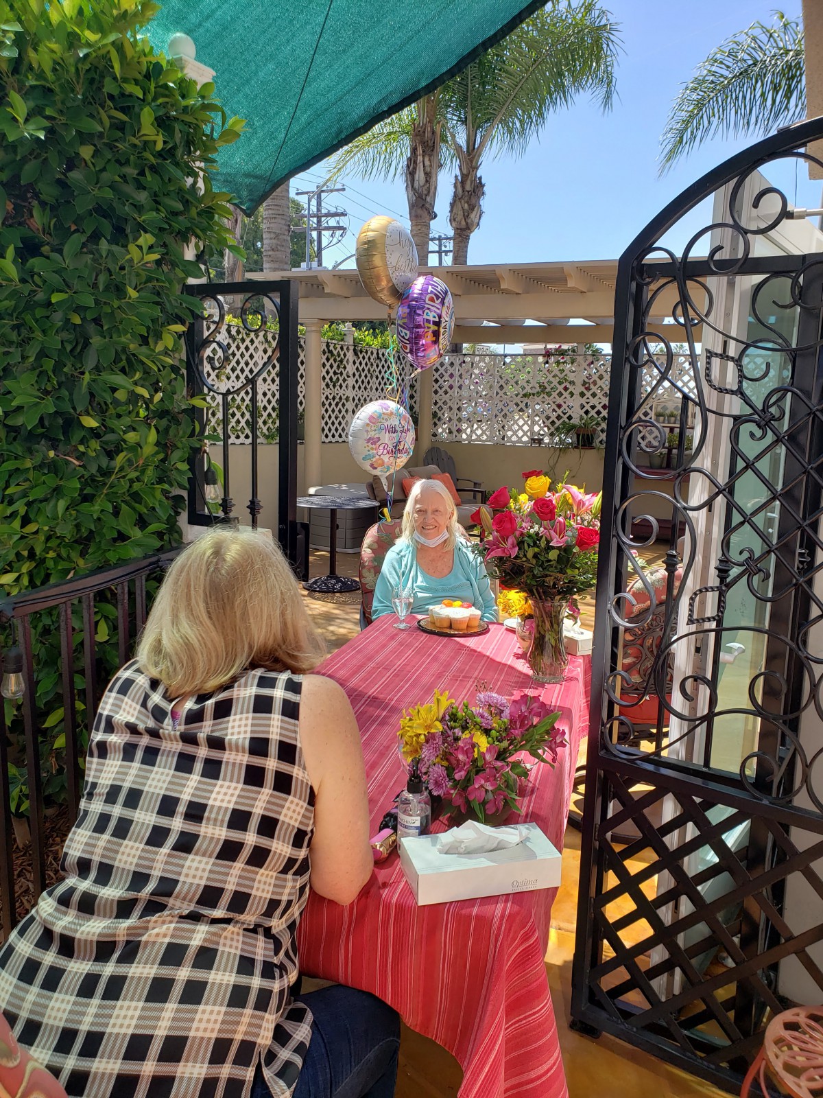 An outdoor birthday celebration with balloons, flowers, and a cake on the table.