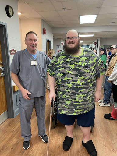 A patient using a walking aid stands alongside a hospital staff member, highlighting the supportive environment in rehabilitation.