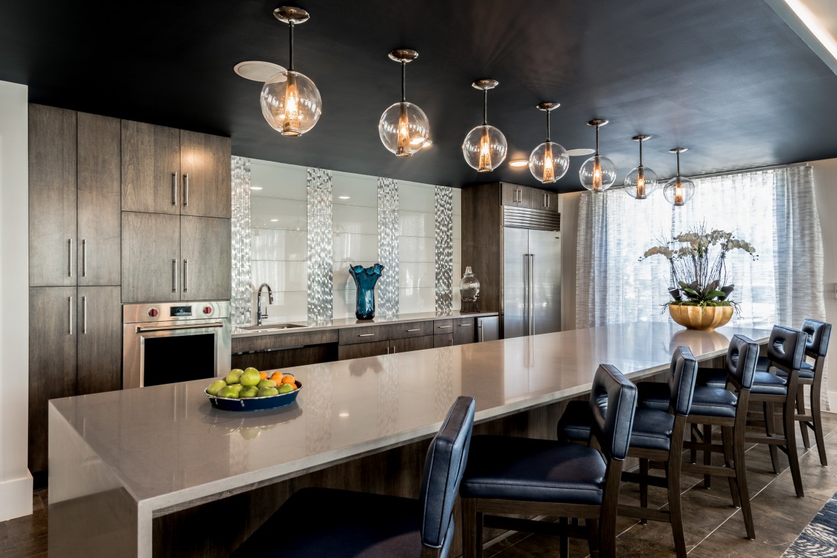 A modern kitchen featuring a long countertop with bar seating and stylish globe pendant lights.