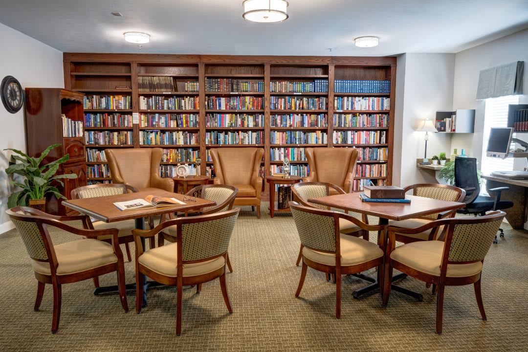 A cozy library reading area with bookshelves, comfortable chairs, and tables.