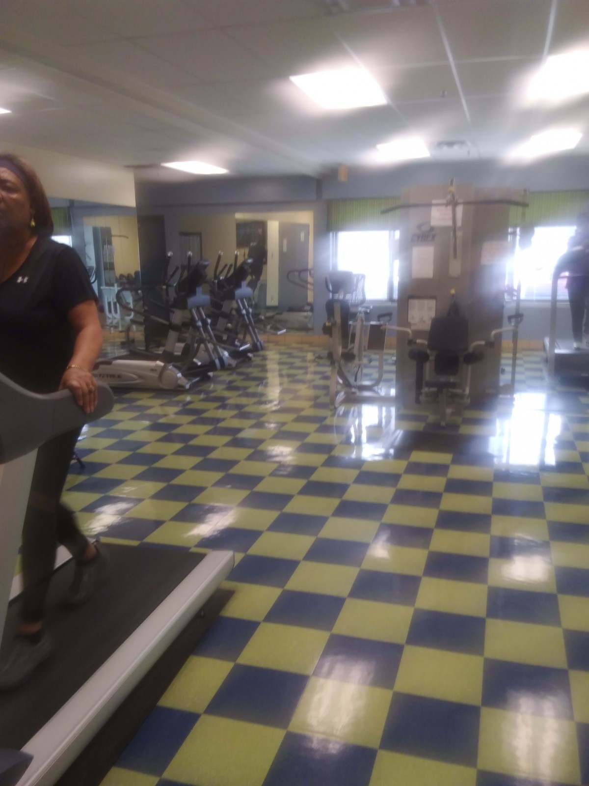 A person exercises on a treadmill in a gym with checkered flooring.