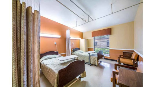 A view of a patient room in a healthcare facility featuring two beds and warm-colored walls.