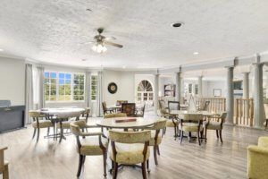 A spacious and bright dining area with multiple tables and chairs, featuring large windows and a ceiling fan.