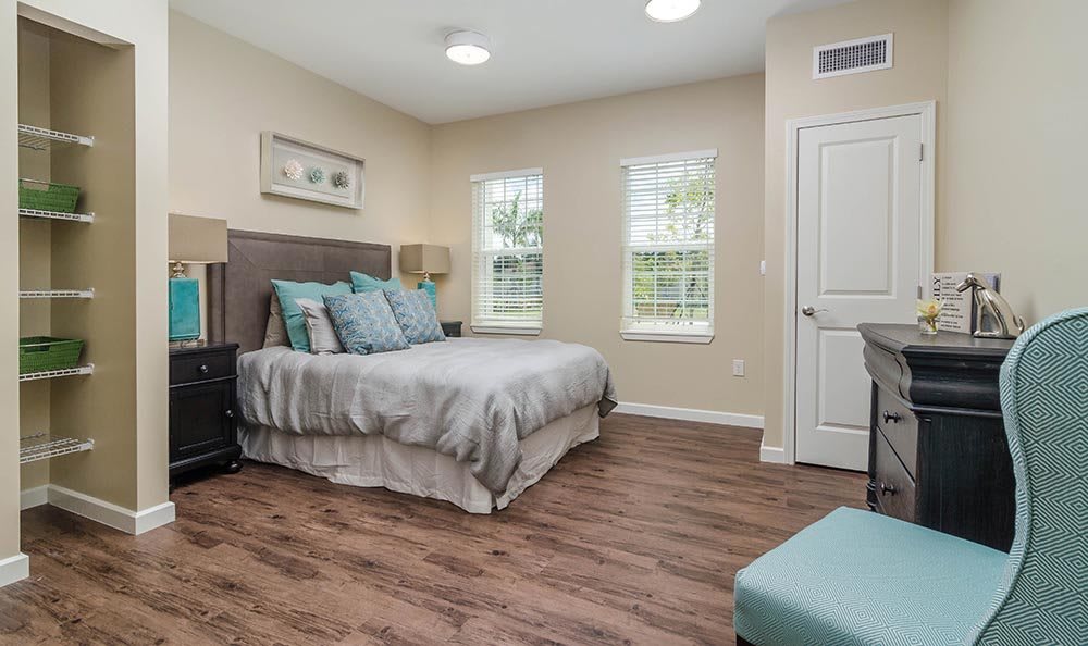 A modern bedroom with a cozy bed, hardwood flooring, and large windows allowing natural light to fill the space.