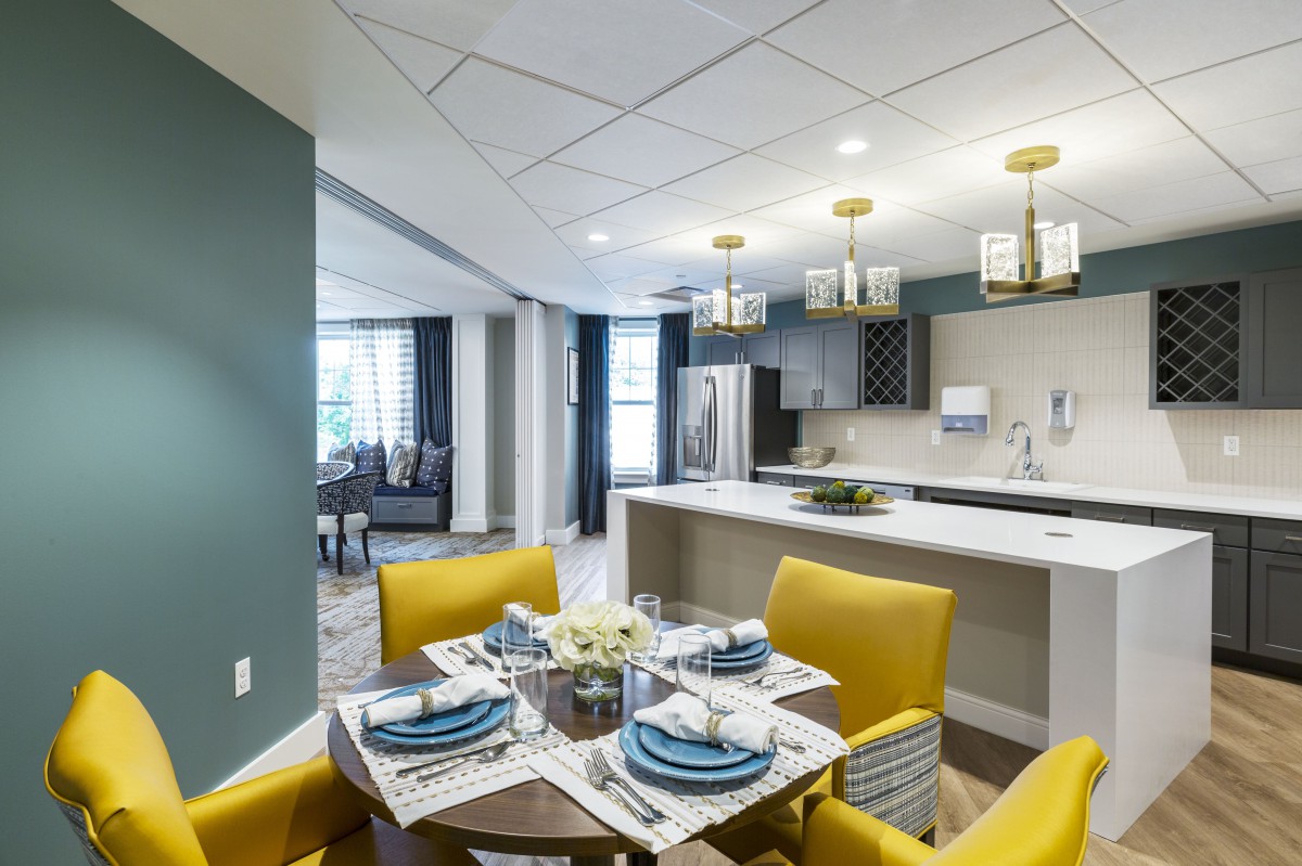 A modern dining room with yellow chairs and an open kitchen, featuring elegant lighting and a stylish table setting.