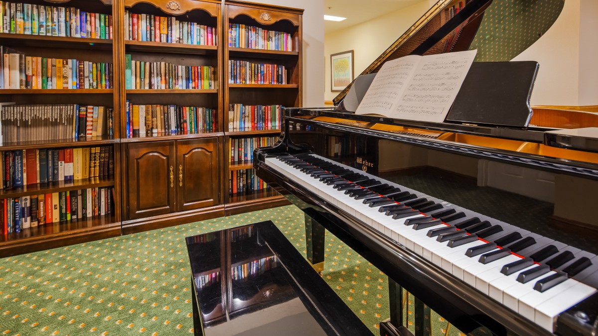 A cozy library room featuring a grand piano and a fully stocked bookshelf.