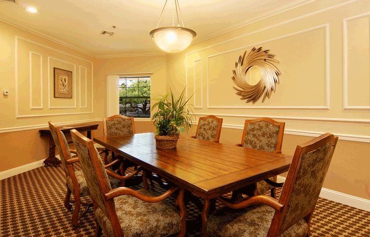A well-appointed meeting or dining room with a large wooden table, elegant chairs, a decorative wall piece, and a potted plant.
