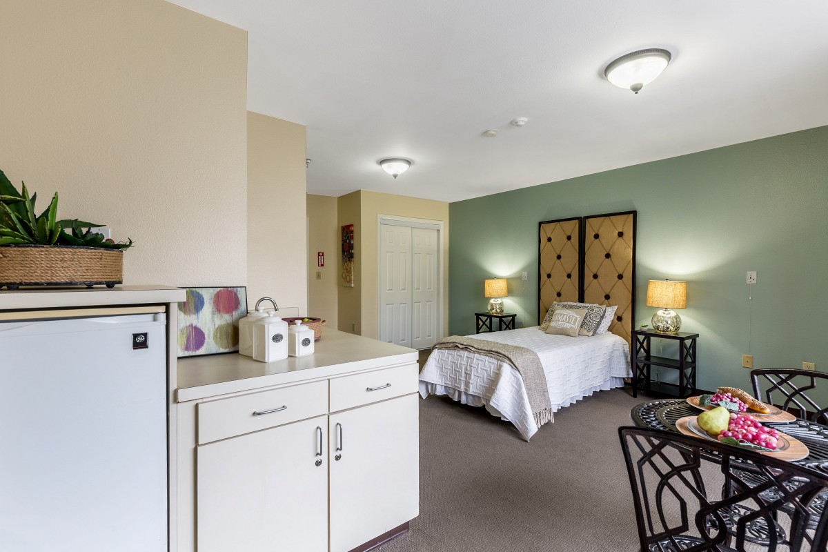 A cozy bedroom with a kitchenette, featuring a bed, nightstands, and lamps.