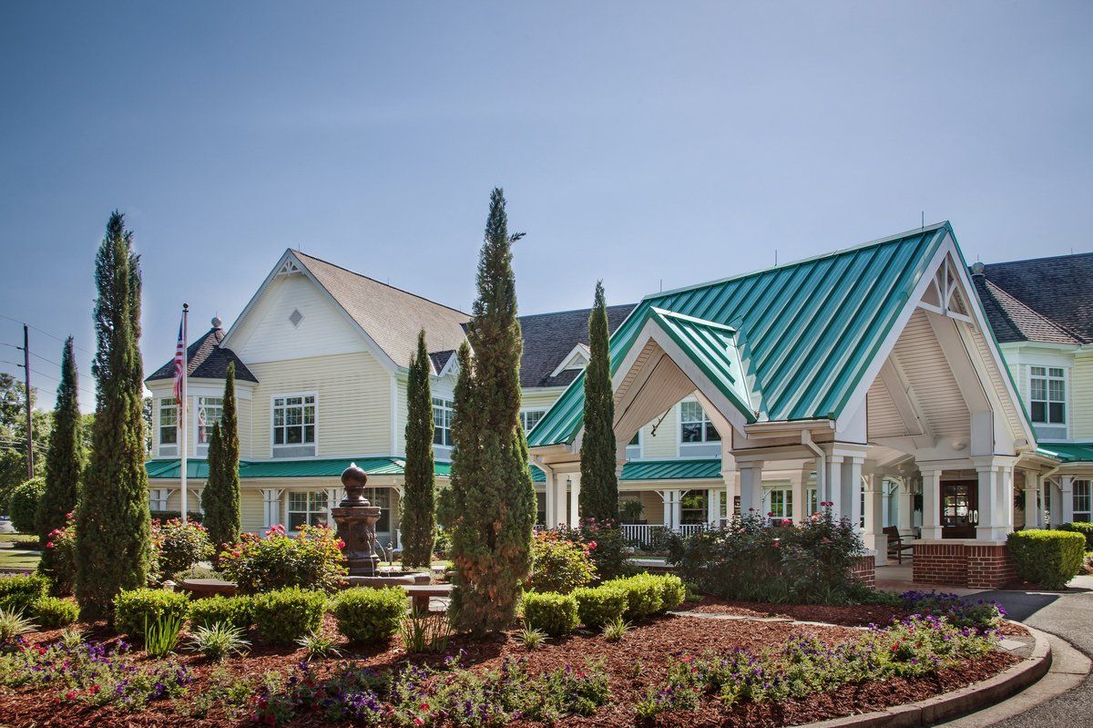 A beautifully landscaped building with a green roof and tall trees on a sunny day.