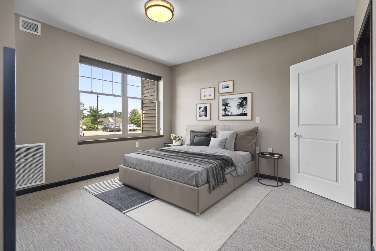 A modern and minimalist bedroom featuring neutral tones, with a neatly made bed and large window allowing natural light to fill the space.