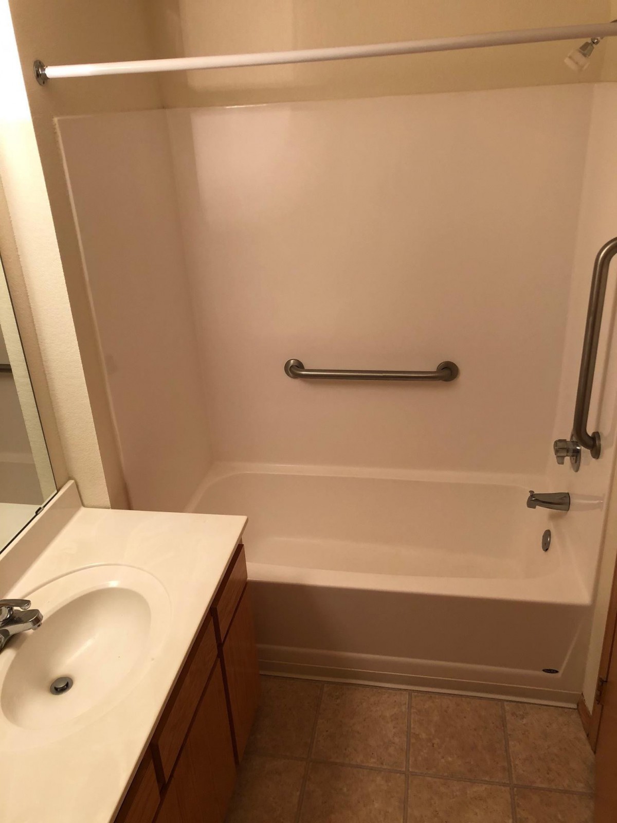 A small bathroom featuring a bathtub with a grab bar, adjacent to a sink and countertop.
