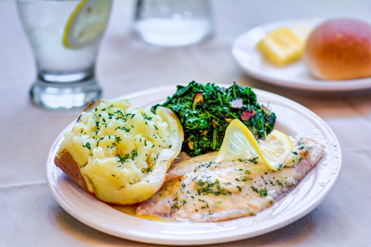 A plated meal featuring fish with lemon slices, sauted spinach, and a baked potato.