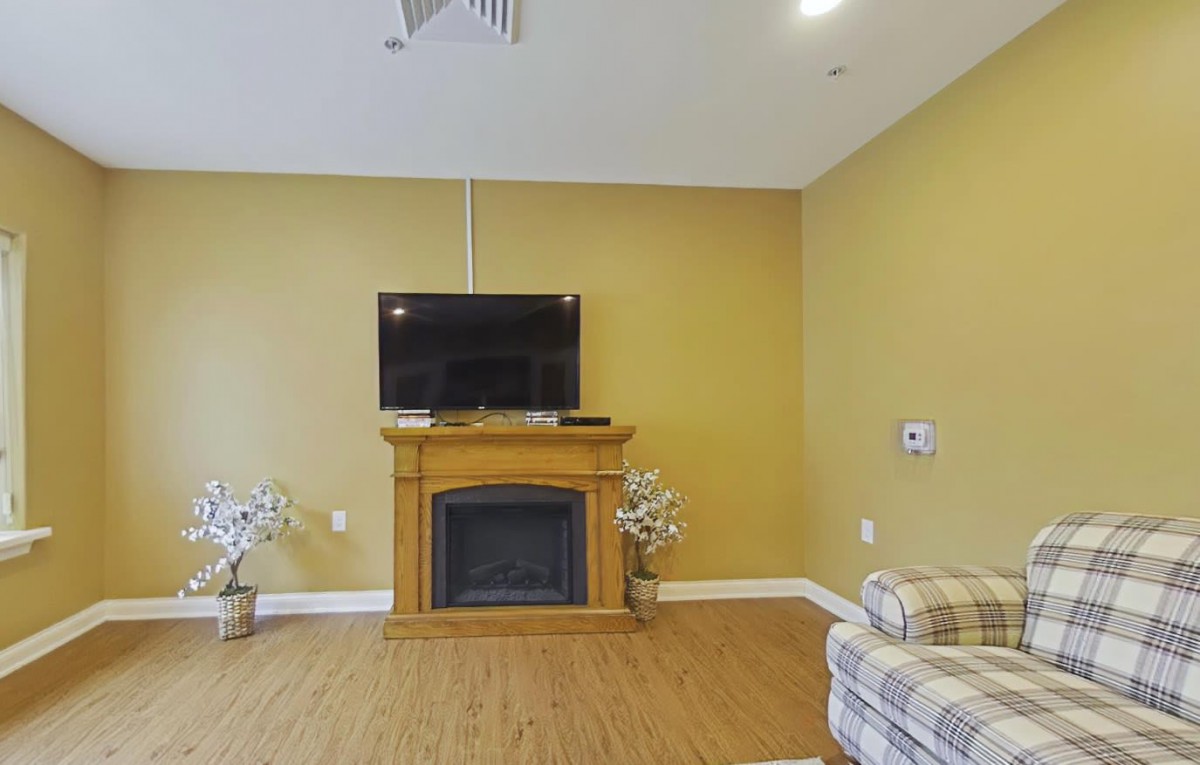 A cozy living room with a wall-mounted television above a wooden fireplace, surrounded by classic decor and a comfortable sofa.