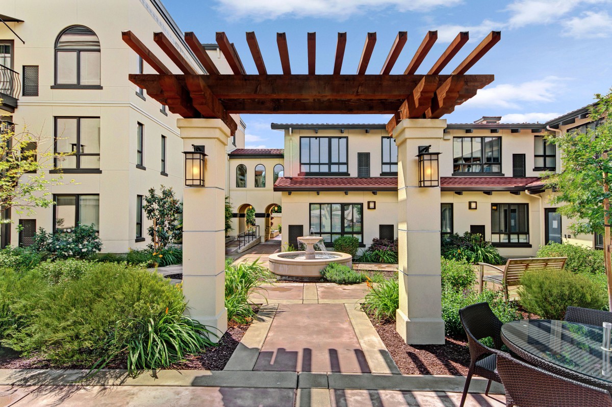A beautifully landscaped courtyard features a pergola and fountain in a sunny residential setting.