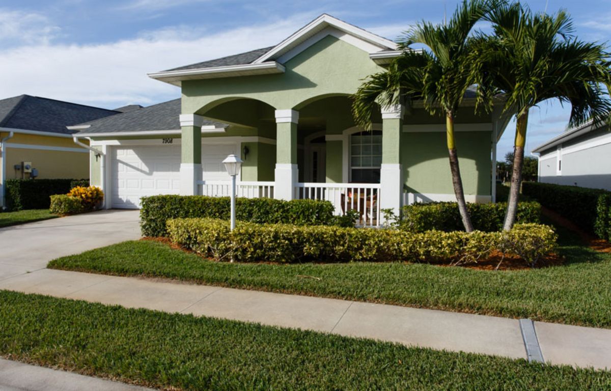 A suburban house with a green exterior, palm tree, and neatly trimmed lawn.