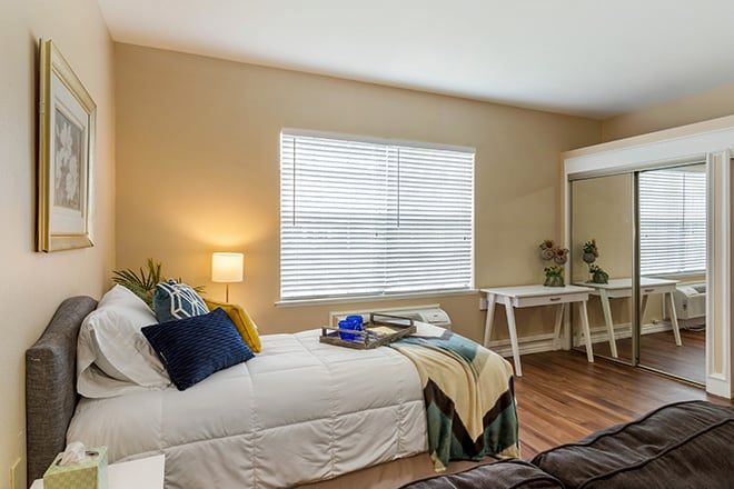 A cozy bedroom with a stylish bed, a desk beside the window, and warm lighting.