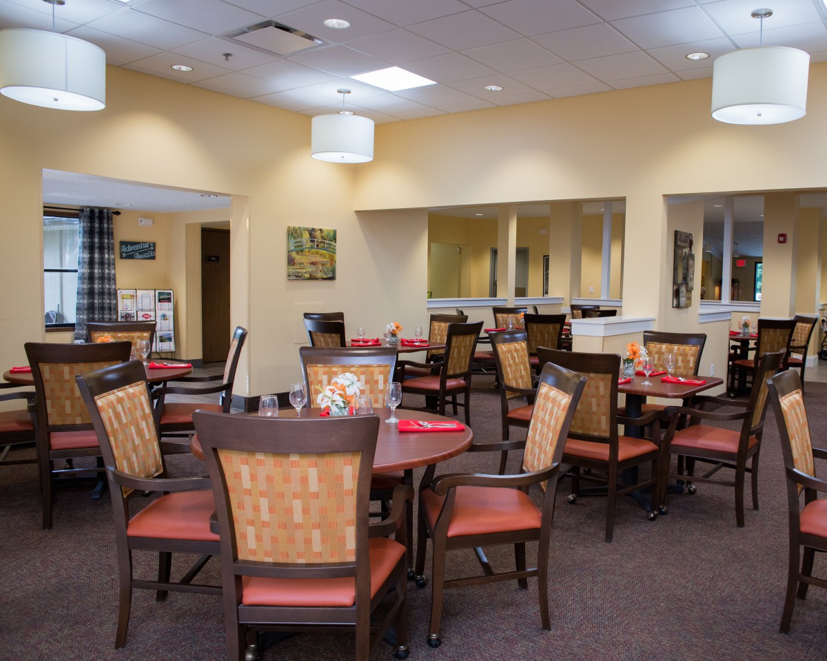A neatly arranged dining room with multiple tables and chairs, featuring warm lighting and a cozy ambiance.
