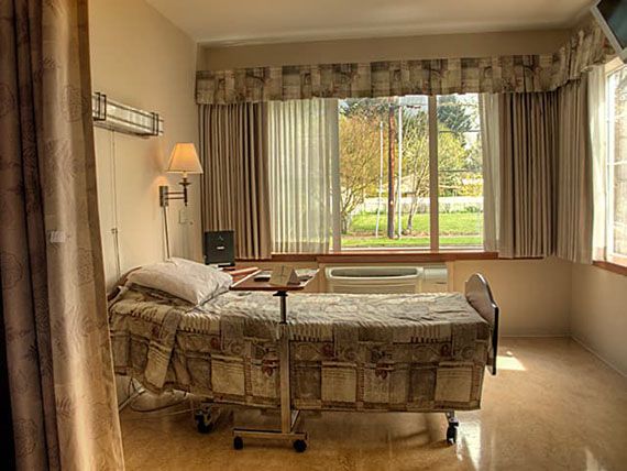A hospital room with a single bed by a large window letting in sunlight.