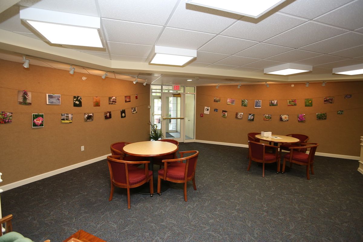 A waiting area featuring round tables with chairs, art displayed on the walls, and a carpeted floor.