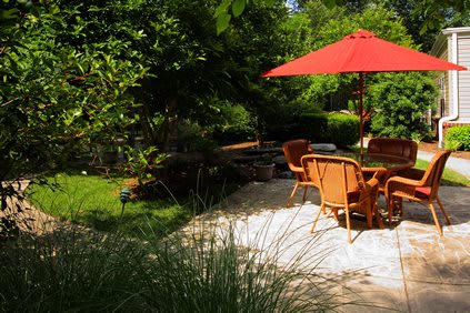 A serene garden patio with chairs and a red umbrella, surrounded by lush greenery.