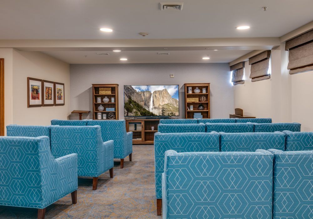 A small theater room with blue upholstered seating and a television at the front.