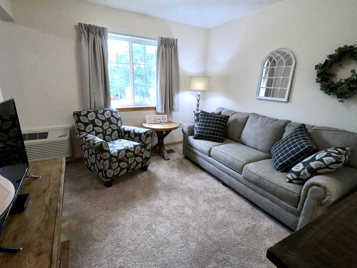 A cozy living room with a sofa, armchair, and a lamp near the window.