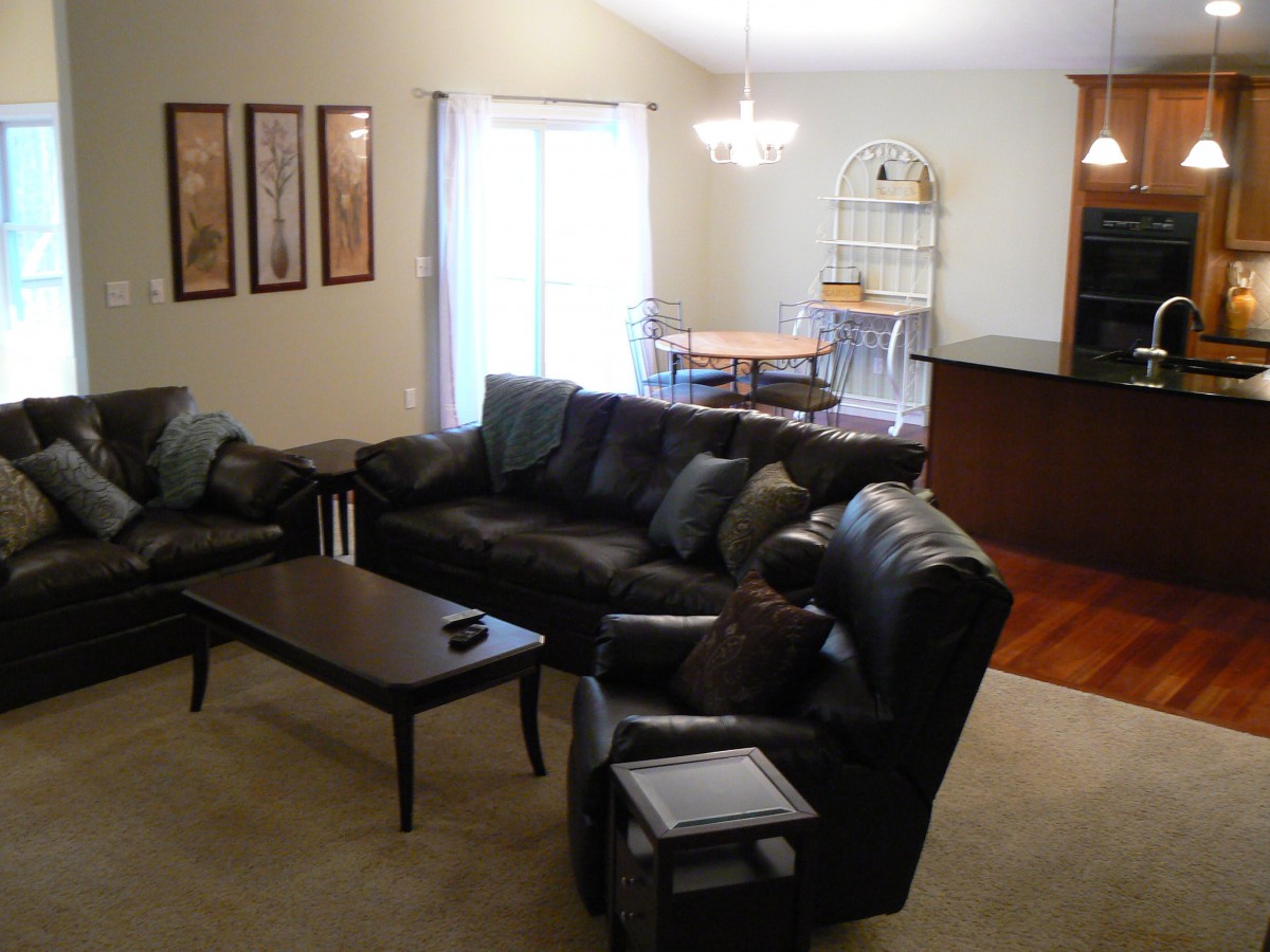 A cozy living room with a black leather sofa set and a coffee table, adjacent to an open dining area.
