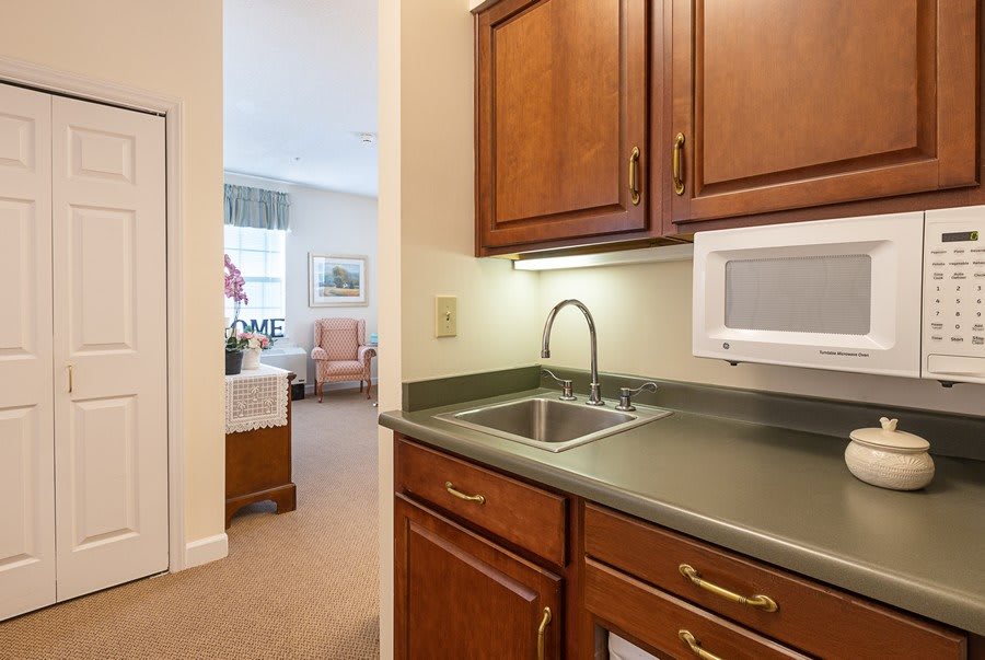 Small kitchenette with wooden cabinets and a sink, leading into a cozy room.