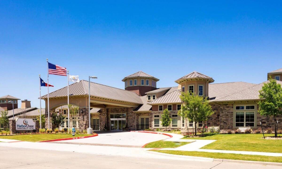 A modern building entrance with landscaping and a flag on a sunny day.