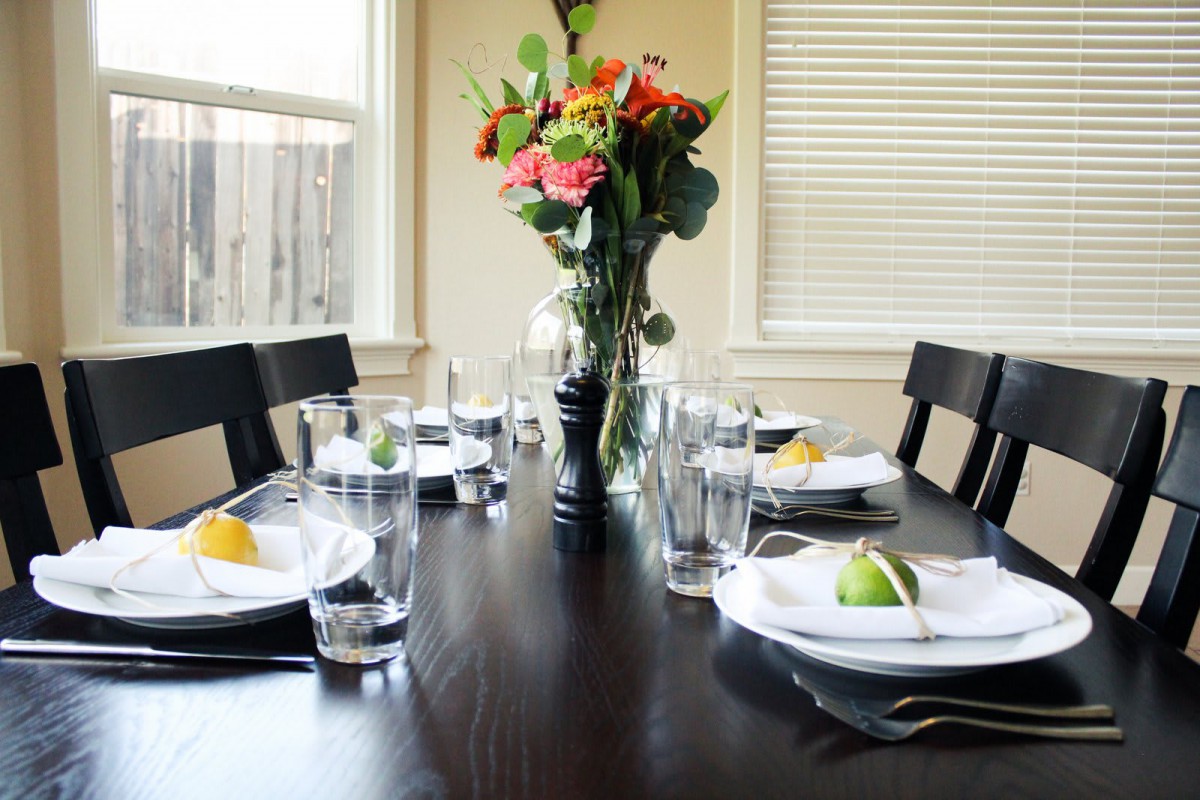 A beautifully set dining table with plates, glasses, and a vase of flowers as the centerpiece.