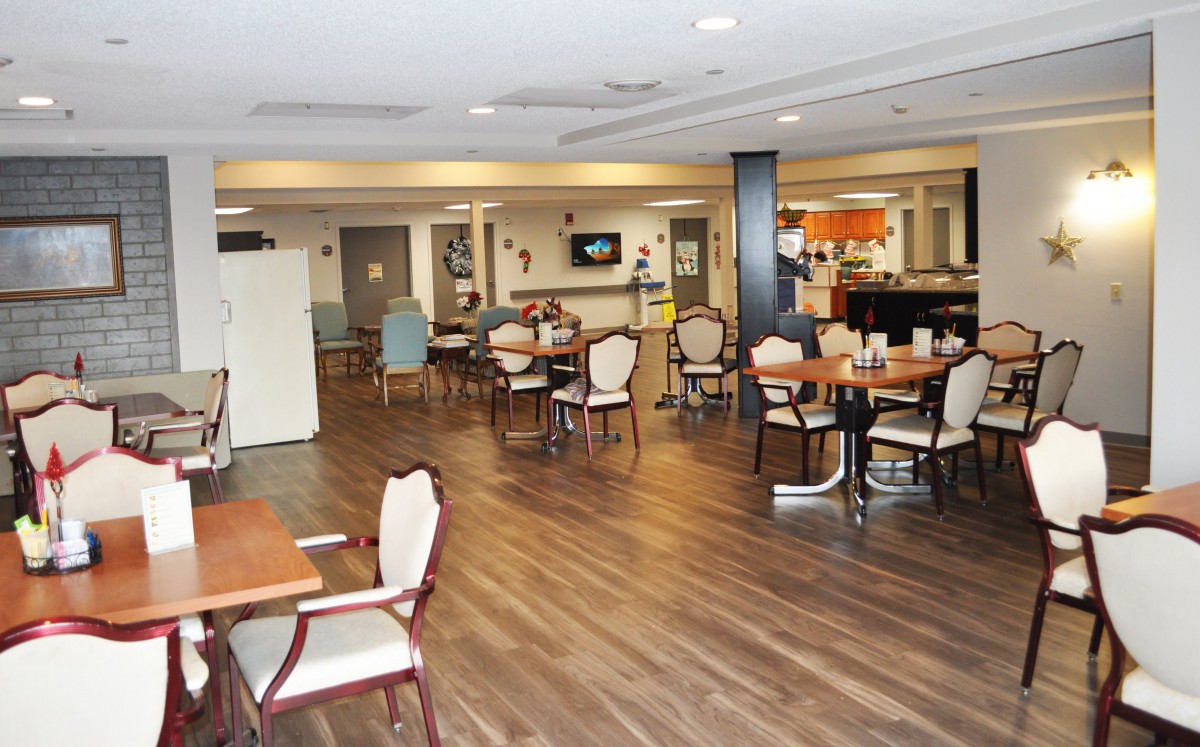 A spacious dining area with wooden flooring and neatly arranged tables and chairs.