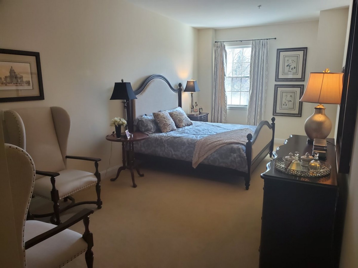 A cozy bedroom with a neatly made bed, armchairs, and ambient lighting.