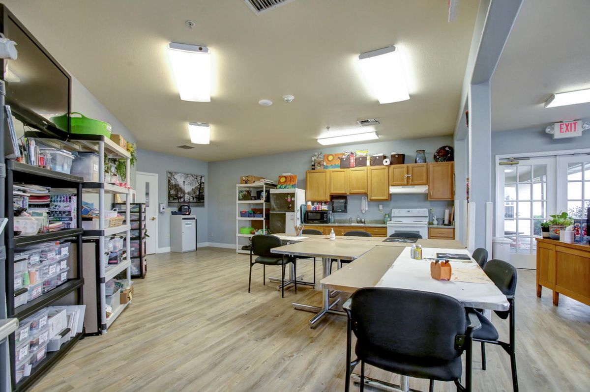 A spacious office meeting area with tables, chairs, shelves, and a kitchenette.