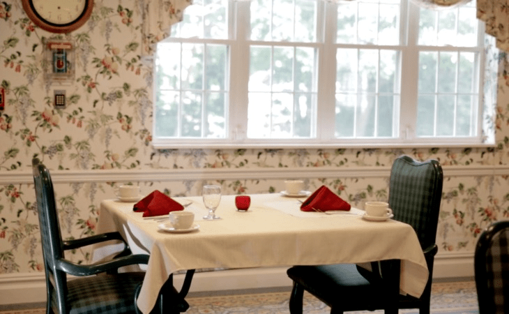 A cozy dining area with a neatly set table, featuring red napkins and natural light streaming through the window.