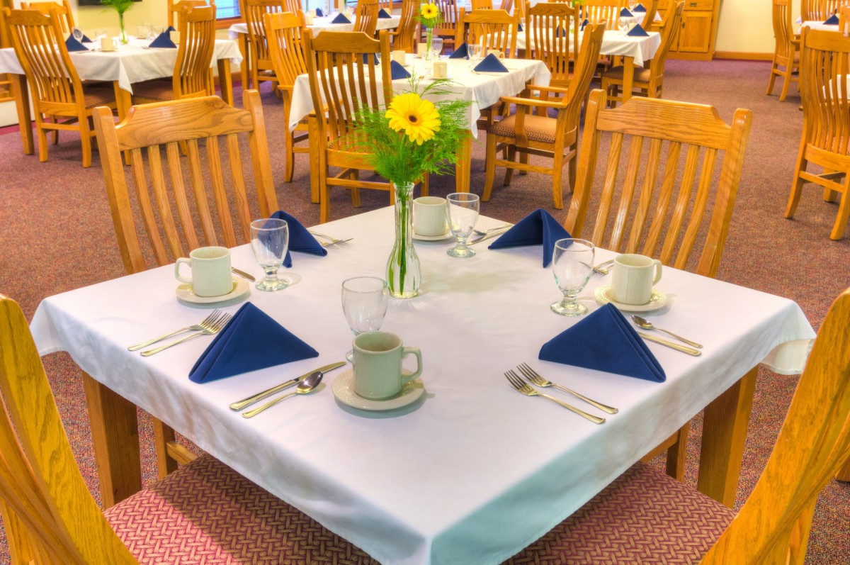 A neatly set restaurant table with blue napkins and a vase of flowers.