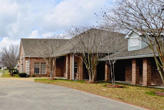 A suburban brick house with a large driveway and trees in the yard.