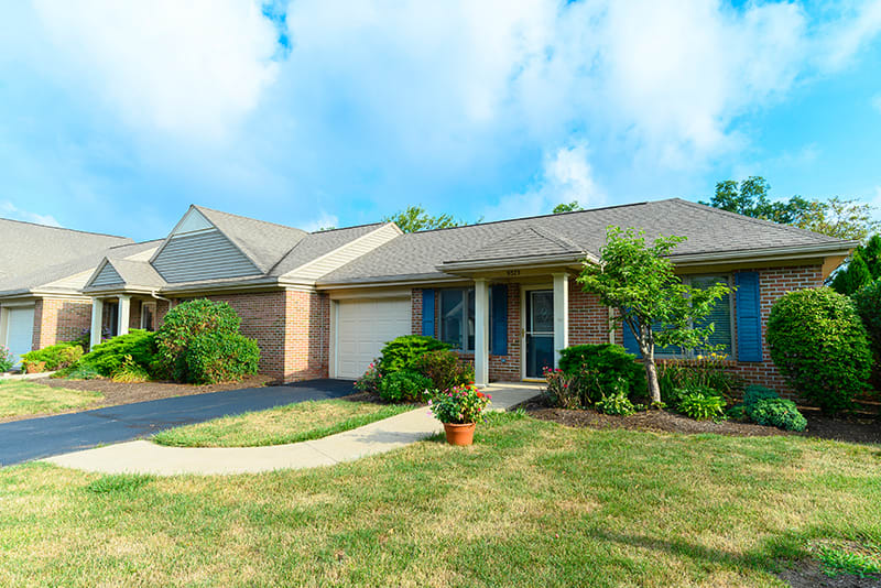 A suburban house with a well-maintained lawn and driveway under a clear blue sky.