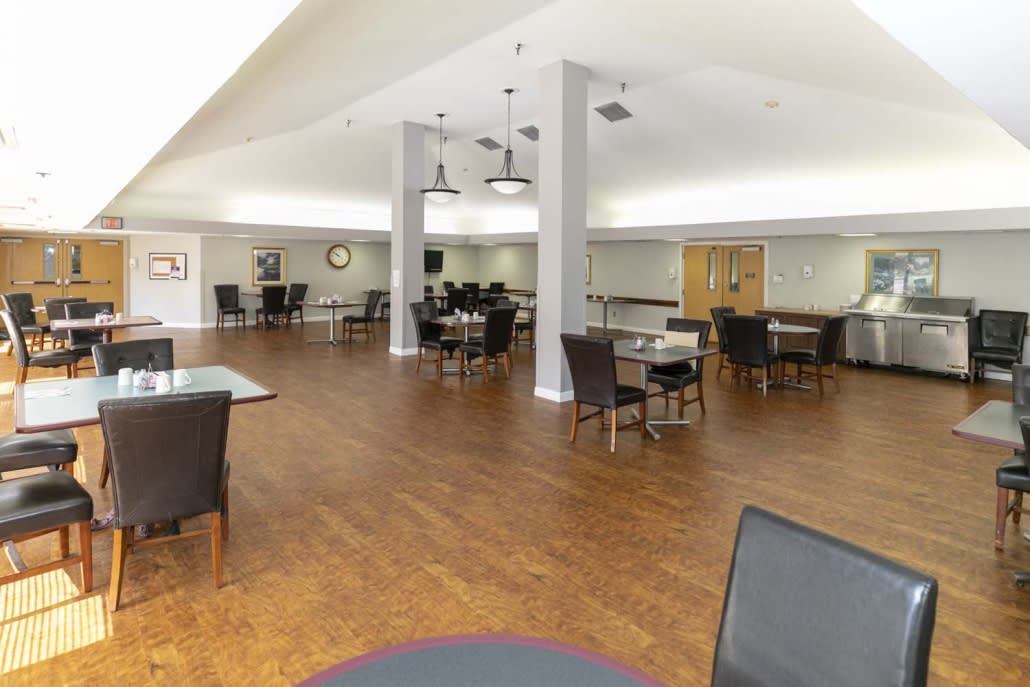 A spacious dining area with tables and chairs arranged neatly on a hardwood floor, illuminated by ceiling lights.