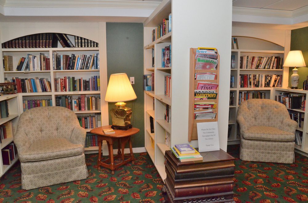 A cozy library reading area with bookshelves, comfortable chairs, and a lamp.