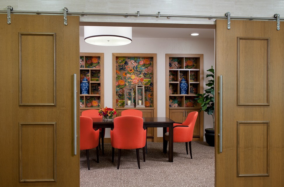 A modern dining room with vibrant red chairs and decorative bookshelves.