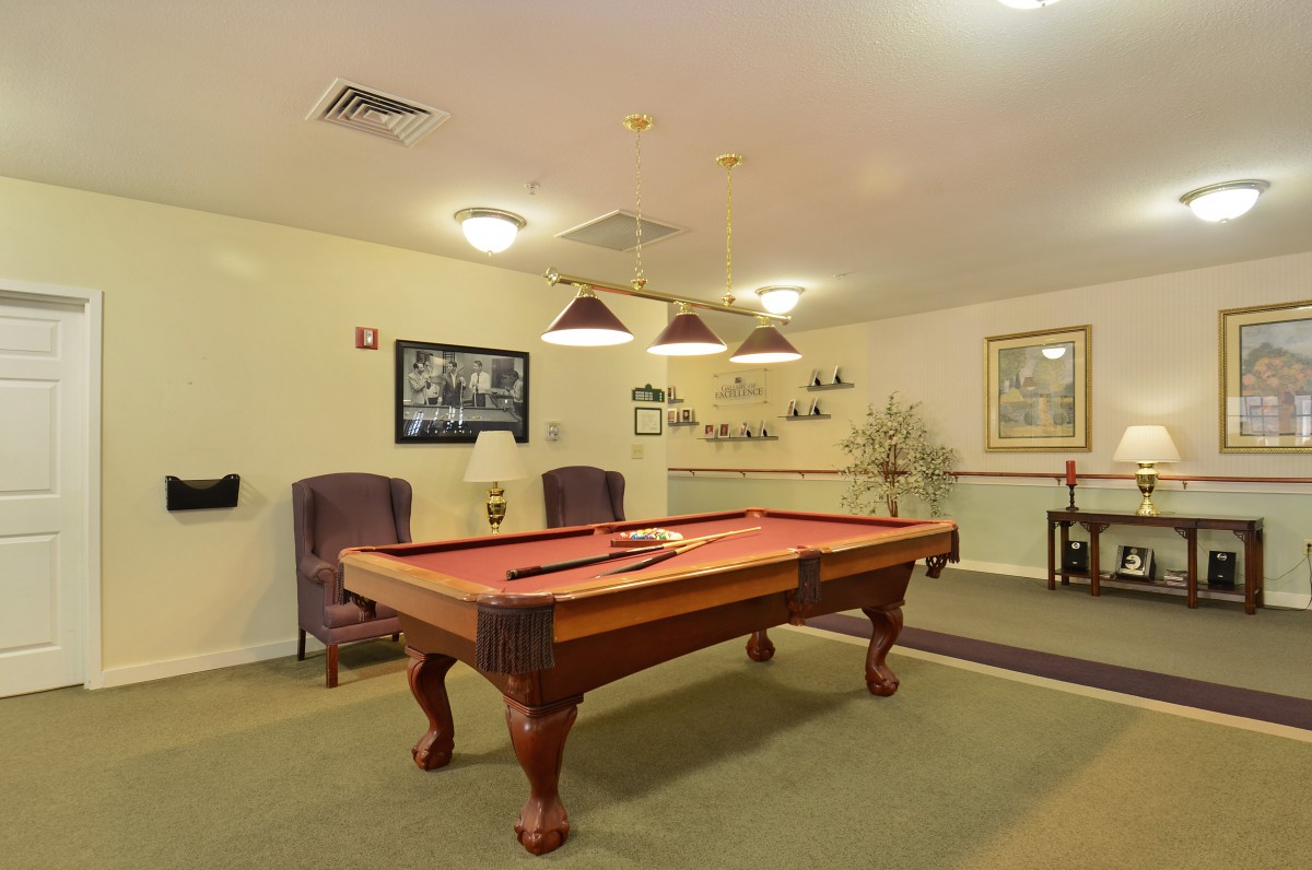 A cozy game room featuring a classic pool table with overhead lighting and comfortable seating.
