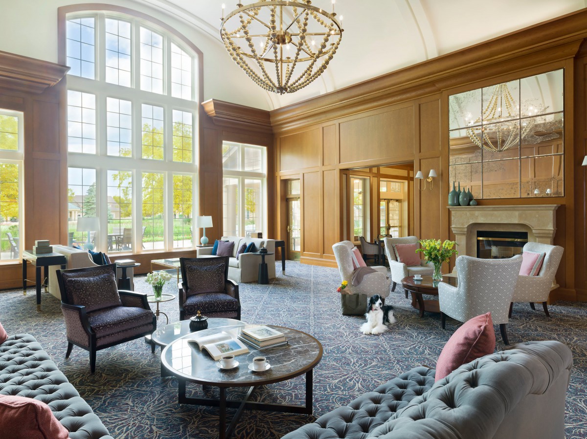 A luxurious and modern living room with large windows, elegant wood paneling, and a central chandelier.