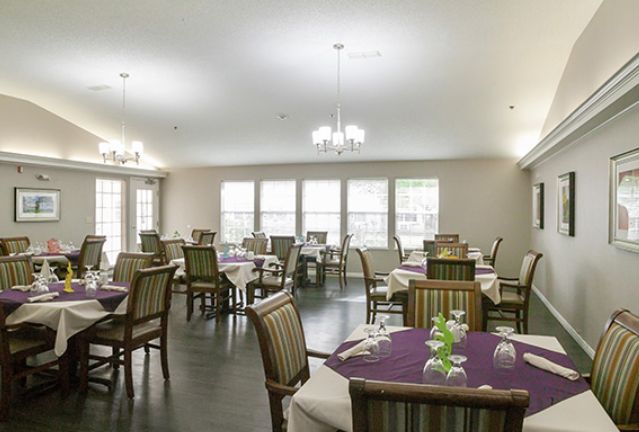 A well-lit dining room with neatly arranged tables and chairs, featuring chandeliers and large windows.