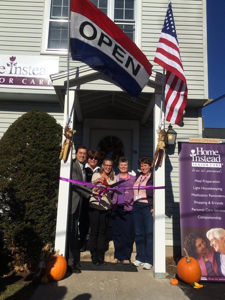 A group of people gathered for a ribbon-cutting ceremony to mark the opening of a business on a sunny day.