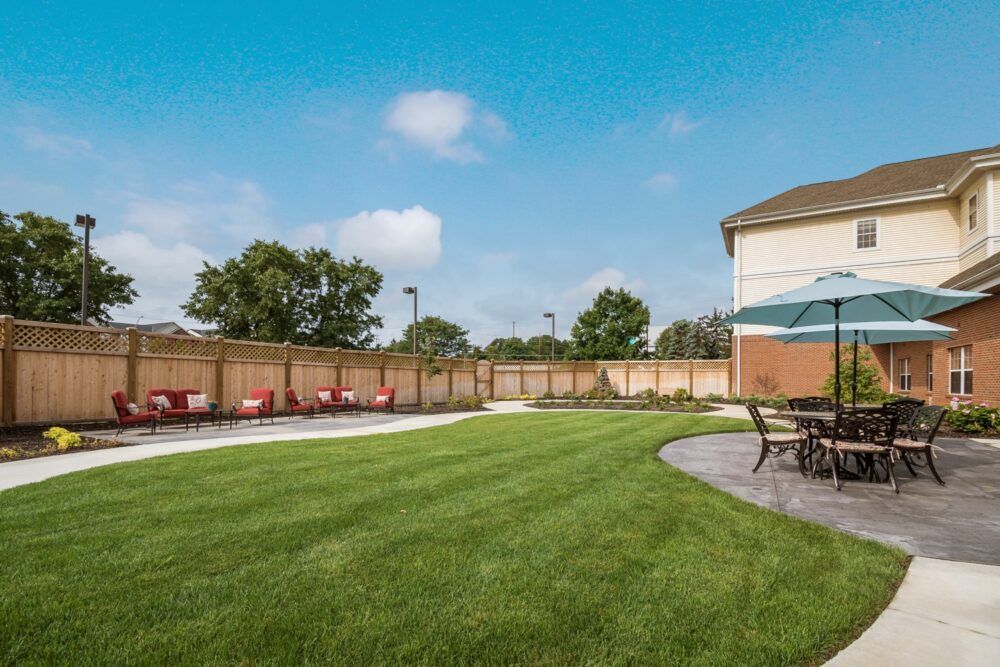 A spacious backyard with a well-maintained lawn, surrounded by a wooden fence, featuring patio furniture and an outdoor umbrella under a clear blue sky.
