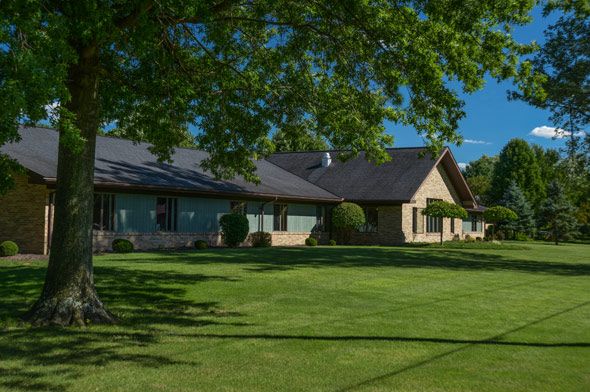 A sunny day view of a residential house with a well-maintained lawn and surrounding trees.