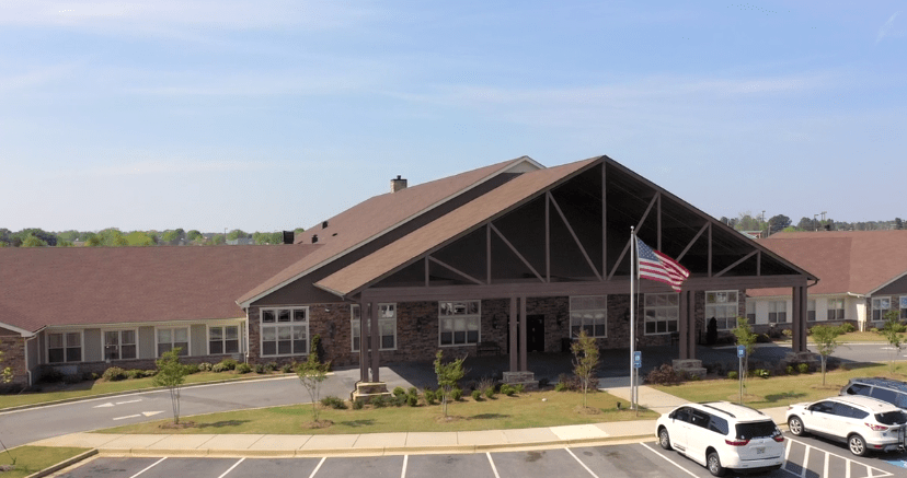 A large building with a prominent roof, an American flag, and a nearby parking lot under a clear sky.