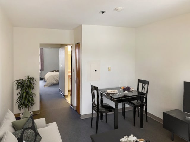 A cozy dining area in a modern apartment, featuring a table set for two and a view into the bedroom.